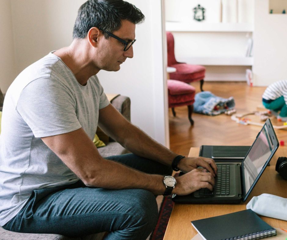 Laptop előtt ülő férfi feszes testtartással, háttérben gyerekszobával